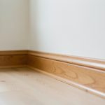Intérieur d’une maison propre et réaliste, inspection des plinthes et boiseries en bois, lumière naturelle douce et textures nettes.
